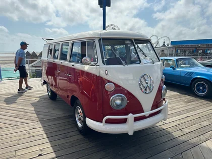 A red-and-white Volkswagen bus on the Wildwood boardwalk with rides in the background