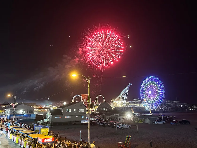 A red firework burst above the illuminated wheel and Wildwood boardwalk at night